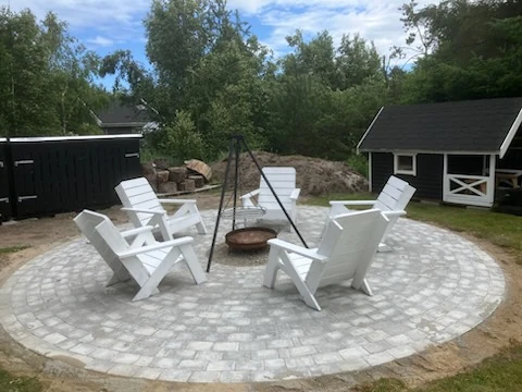 Cirkulær bålplads i betonsten med hvide havestole omkring bålfadet